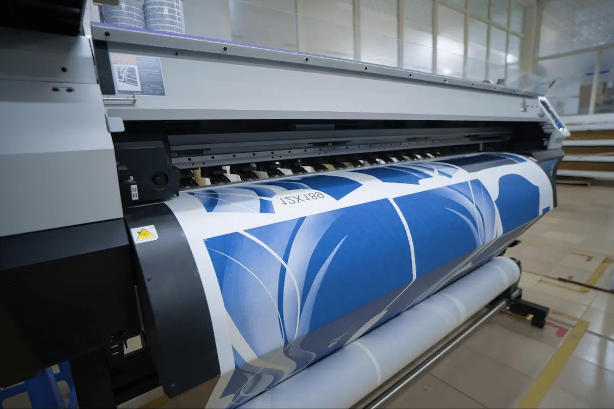 Impressora de grande formato em operação realizando sublimação digital em tecido, com padrões azuis e detalhes brancos.